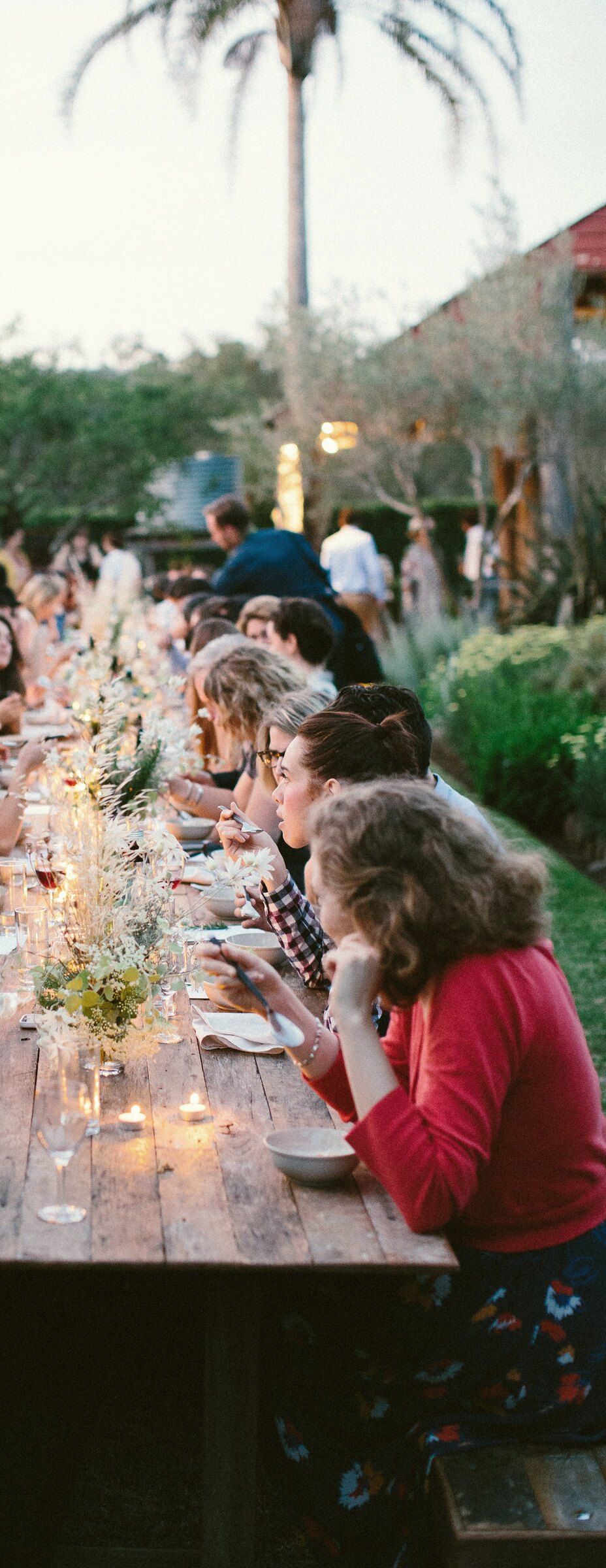 Women gathered at a long candlelit table in a garden at dusk