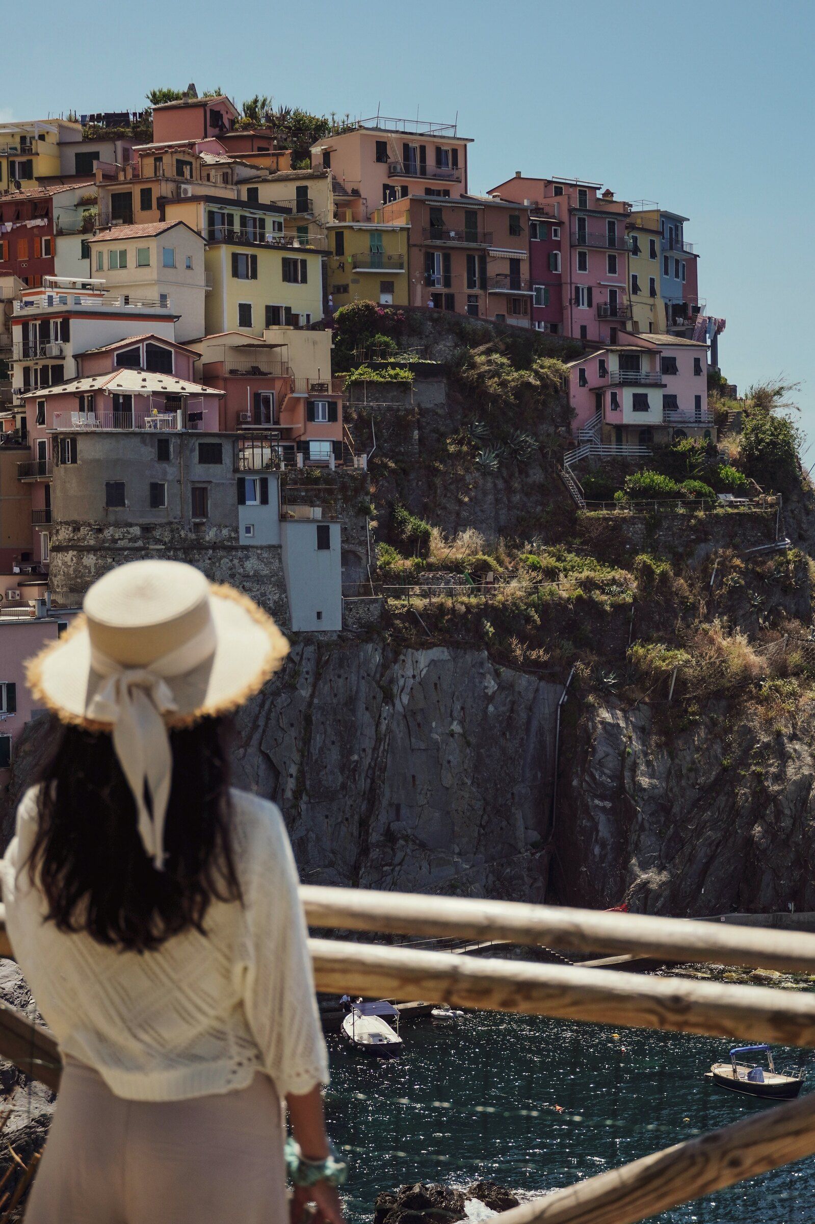 A woman in a sun hat looking out over the pastel cliffside village of Manarola