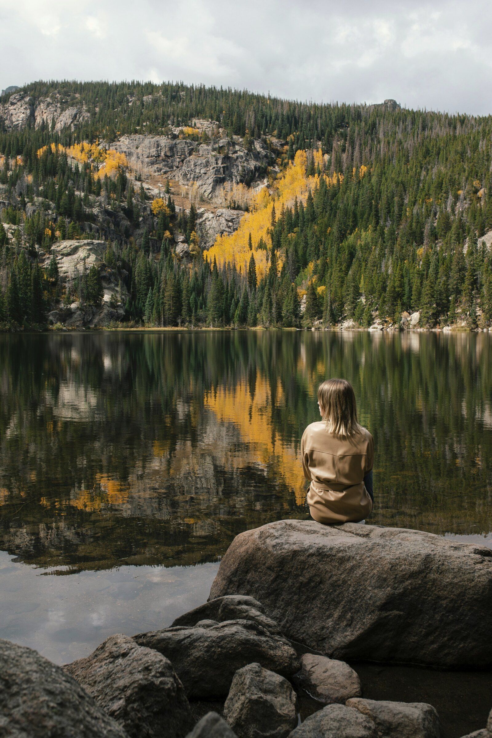 A woman sitting on a boulder at an alpine lake ringed with golden aspens
