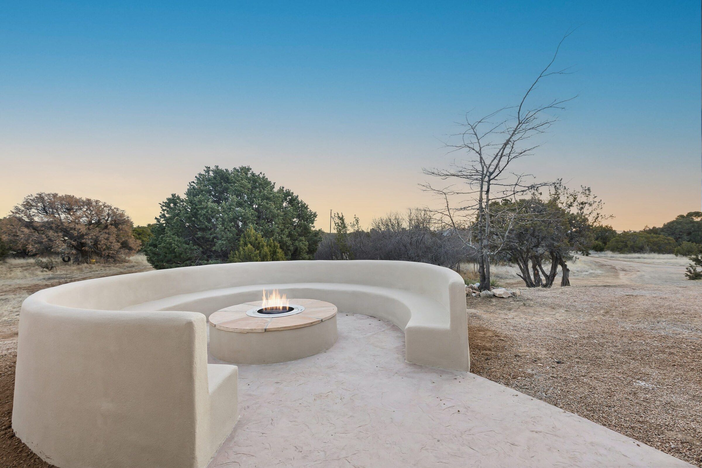 A curved adobe bench around a fire at dusk in the Santa Fe high desert